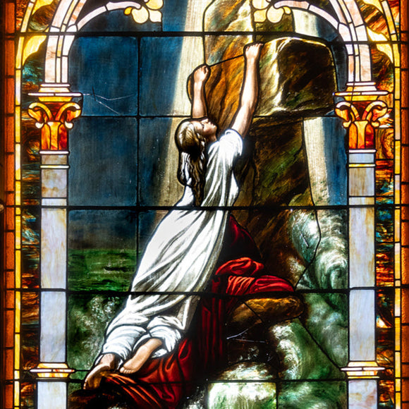 Stained glass window with religious scene, featuring a figure in a robe and a cross.